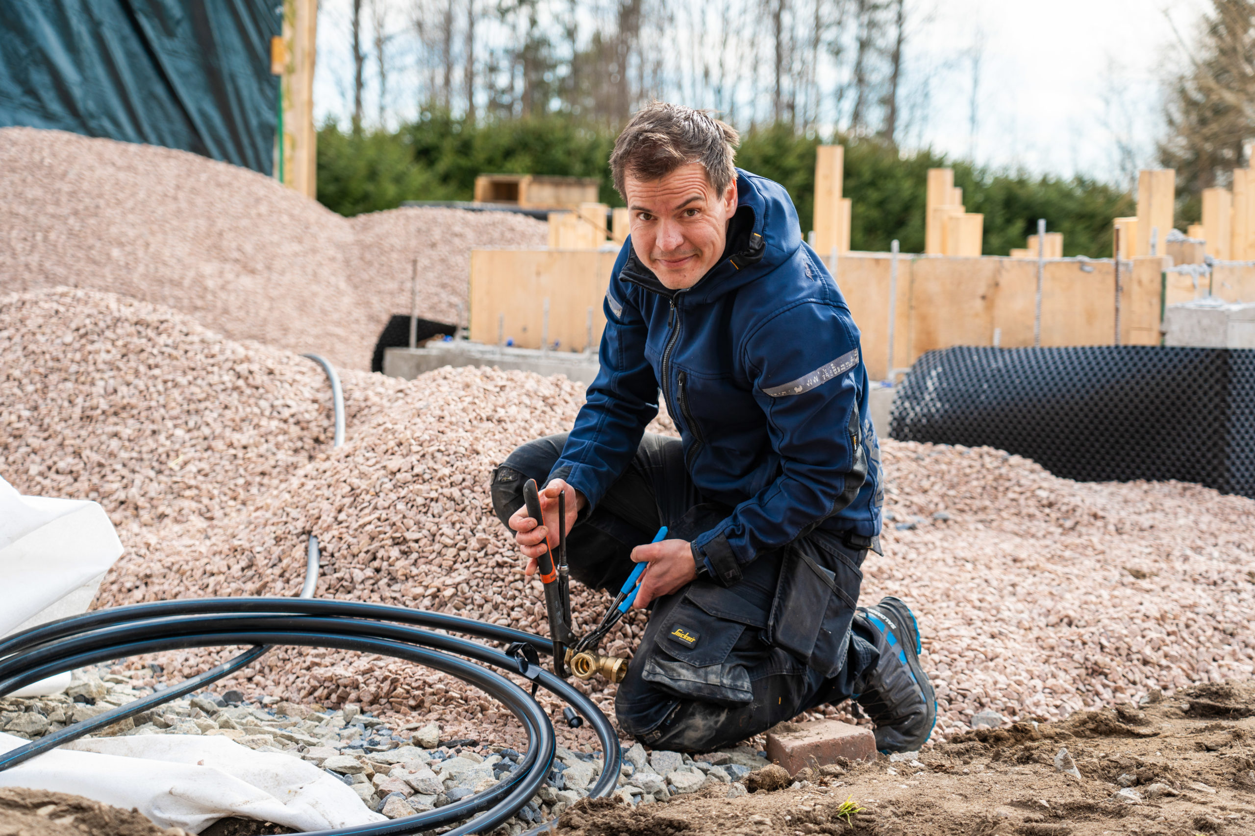 Even Sandvoll sitter på huk og skrur på en vannledning i bakken.